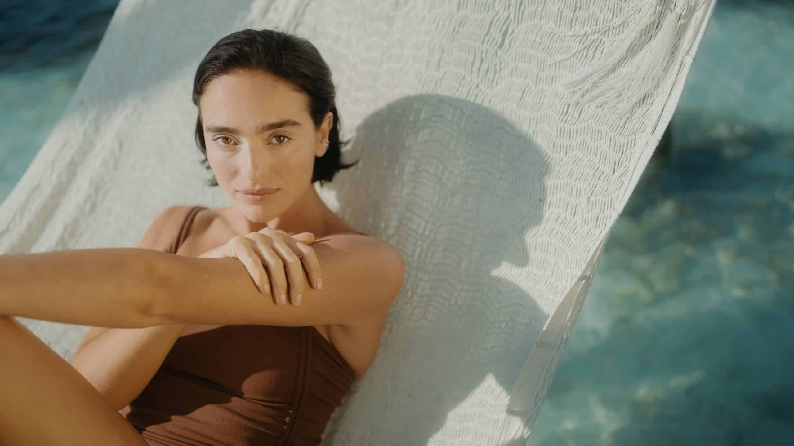 Woman in brown one-piece swimsuit relaxing on a white hammock at Mandarin Oriental Residences and Resort at Kanai.